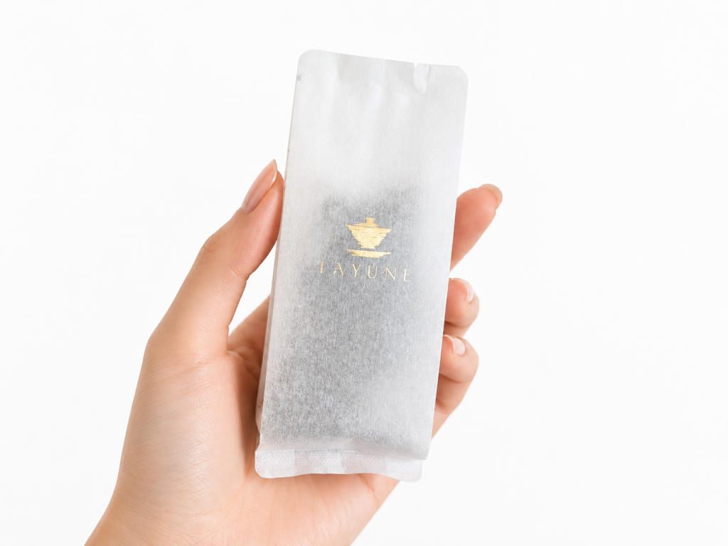 Hand holding one 10 g TAYUNE Pu-erh tea sample sachet